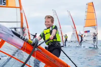 ferienlager-ostsee ein-junge-holt-den-mastbaum-vom-surfbrett-hoch