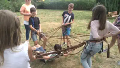 Kinder tragen in einem Spinnennetz aus Seilen ein Kind.