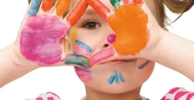 ein kind mit kunterbunten Händen vorm Gesicht