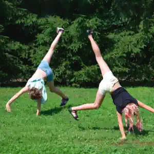 zwei Mädchen schlagen Rad auf der Wiese im Outdoor Camp