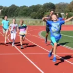 sportcamp-fun mehrerre Kinder rennen auf der Tartar-Bahn einen Wettlauf