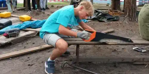 ein Junge sägt ein Brett für das Baumhaus