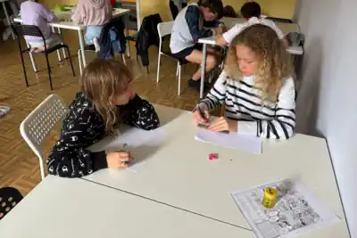 am Tisch sitzen zwei Mädchen und lernen im Ferienlager-Englischcamp für 12-jährige